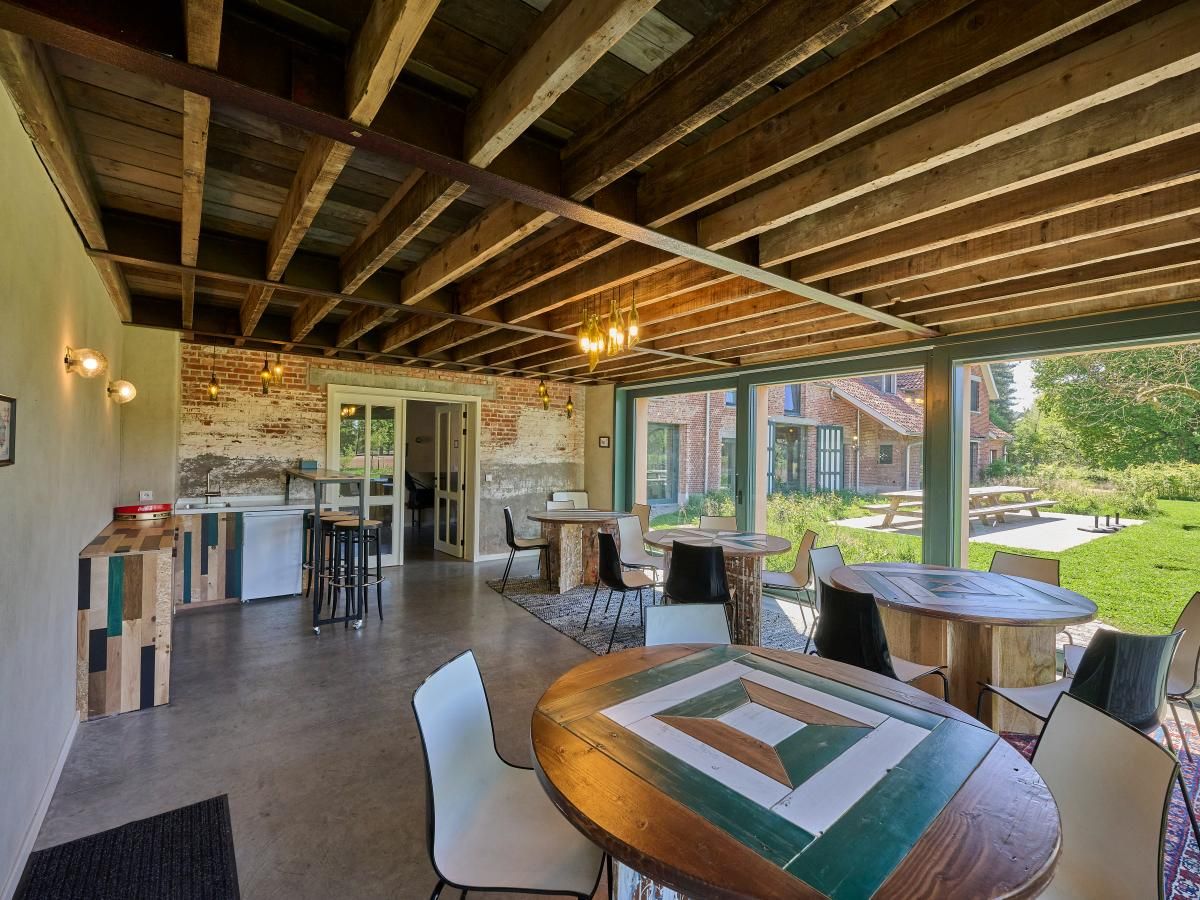 Binnenruimte van vakantiehuis Lactea in Schilde, Antwerpen met rustieke houten balken en uitzicht op groene tuin.