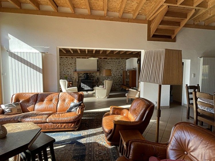 Gezellige woonkamer van La Vallade vakantiehuis in Le Bourg-d'Hem, Limousin met comfortabele leren banken en rustieke stenen muren.