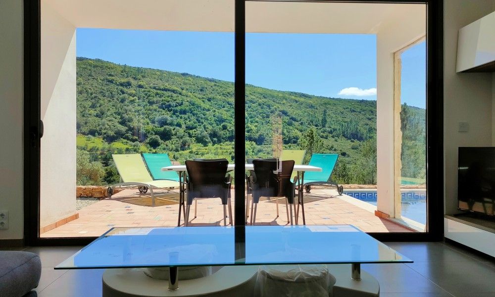 Geniet van het uitzicht op de groene heuvels vanaf de woonkamer van Casa Bananeira villa 4P + baby in Sao Bartolomeu de Messines, Algarve.