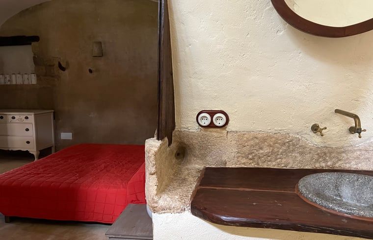 Authentieke slaapkamer in Vakantiehuisje in Navata, Costa Brava, Spanje met rustieke wastafel en rode bedsprei.