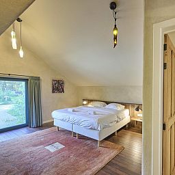 Sfeervolle slaapkamer in Villa Lactea, vakantiehuis in Schilde, met houten vloer en grote ramen.