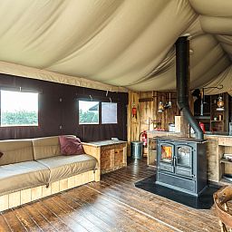 Gemuetlicher Innenbereich des "Tenthuisje" mit warmer eigener Dusche in Beccles, England, mit Holzofen und gemuetlicher Sitzecke.