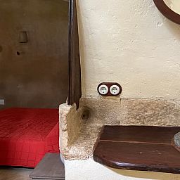 Authentieke slaapkamer in Vakantiehuisje in Navata, Costa Brava, Spanje met rustieke wastafel en rode bedsprei.