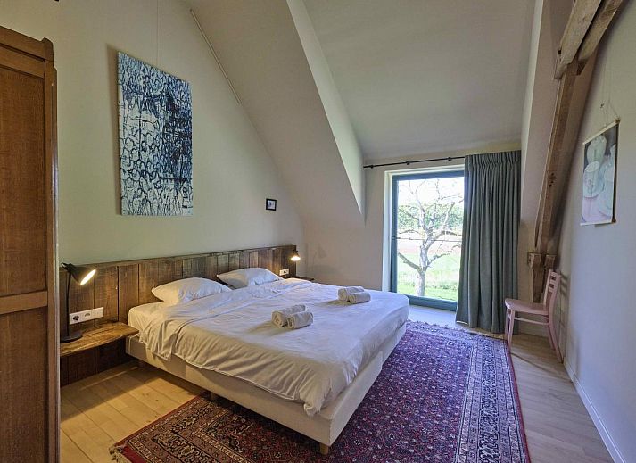 Sfeervolle slaapkamer in Villa Lactea, vakantiehuis in Schilde, met houten vloer en grote ramen.