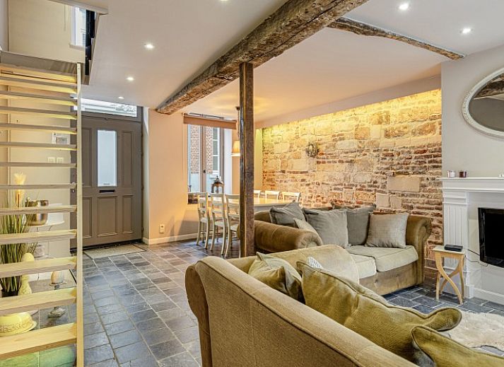 Gemuetliches Wohnzimmer des Ferienhauses Bibi Tongeren in Limburg, Belgien, mit rustikaler Steinwand und bequemer Sitzecke.