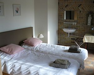 Slaapkamer met twee bedden en bakstenen muur in De Clincke vakantiehuis, Westrozebeke, West-Vlaanderen.