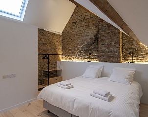Sfeervolle slaapkamer met bakstenen muur in Meet Enjoy vakantiehuis, Nieuwpoort.
