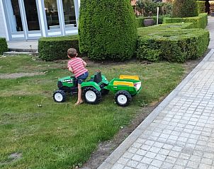 Kind speelt in de tuin van Hoeve Hoogeind, Sint-Gillis-Waas, met speelgoedtractor, een gezinsvriendelijke vakantiewoning in Oost-Vlaanderen.