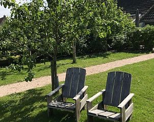 Restful garden of vacation home Castor in Oosterend, Terschelling, with wooden chairs under a tree.