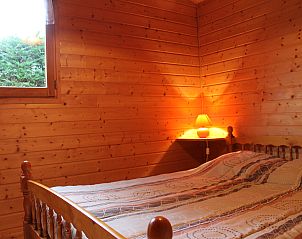 Gezellige houten slaapkamer in Chalet de Pche, Salldes, met warme verlichting en uitzicht op de natuur in Auvergne, Frankrijk.