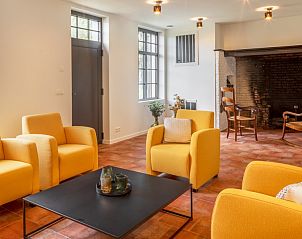 Gezellige woonkamer van Mushoeve in Zoersel, Antwerpen met open haard en comfortabele gele stoelen.