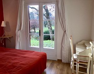 Bedroom in vacation home La Fageole in Domme, Aquitaine, overlooking green nature through large windows.