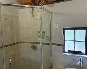 Modernes Badezimmer in unserem Ferienhaus Blyplek, Marloth Park, Sdafrika, mit Glasdusche und rustikalen Strohdachdetails.