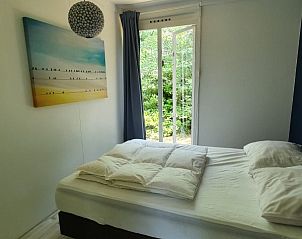 Slaapkamer van vakantiehuis Jutta in Nunspeet, Veluwe, met groot raam en uitzicht op groene natuur, ideaal voor rust en ontspanning.