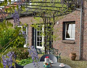 Cozy terrace at Holiday home in Melick, Limburg with sitting area under flowering pergola.