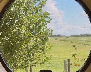 Uitzicht op groene velden door rond raam in Huisje in Oud Ade vakantiehuis in Groene hart Zuid-Holland.